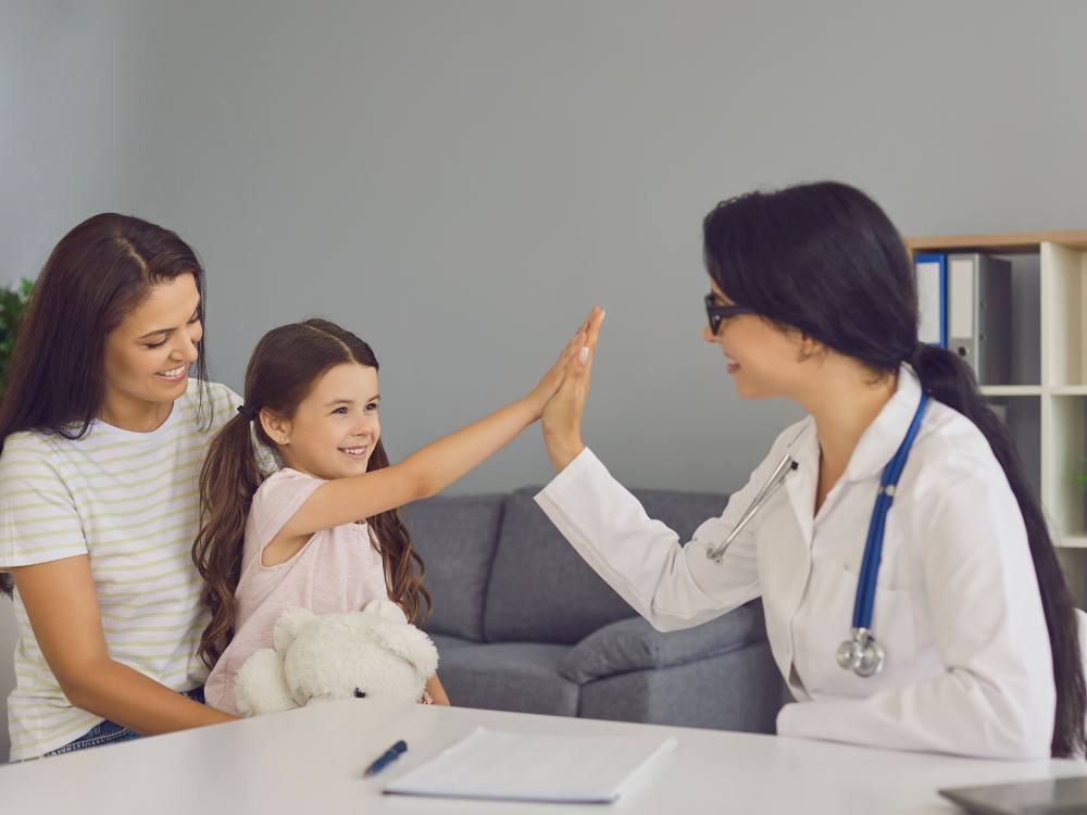 Doctor high-fiving happy child while mom smiles approvingly